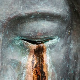 Gesicht einer Skulptur mit geschlossenen Augen und Tränen aus Rost