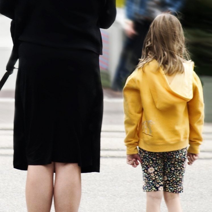Kind mit gelber Jacke steht neben Frau in schwarzer Kleidung