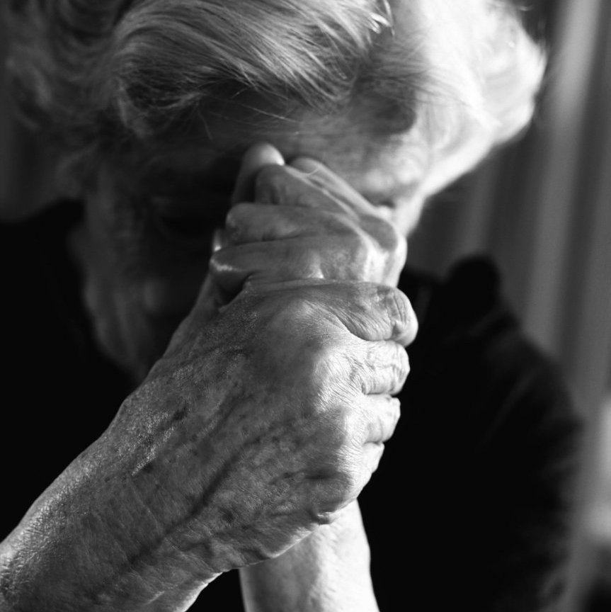 Ältere Frau senkt den Kopf in ihre ineinanderfassenden Hände