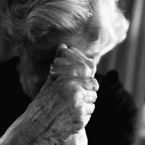Ältere Frau senkt den Kopf in ihre ineinanderfassenden Hände