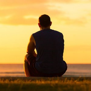Mann sitzt allein im Sonnenuntergang am Meer