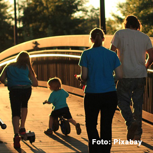 Familie mit Eltern und zwei Kindern geht im Gegenlicht auf eine Brücke zu